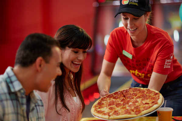 Female server in red shirt setting pepperoni pizza on table.